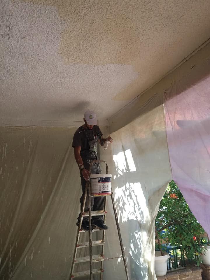 عامل على سلم يطلي السقف بالأبيض