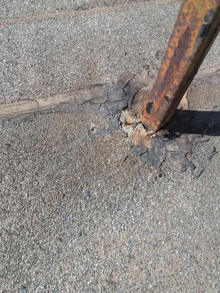 A rusted steel post with torn membrane around it